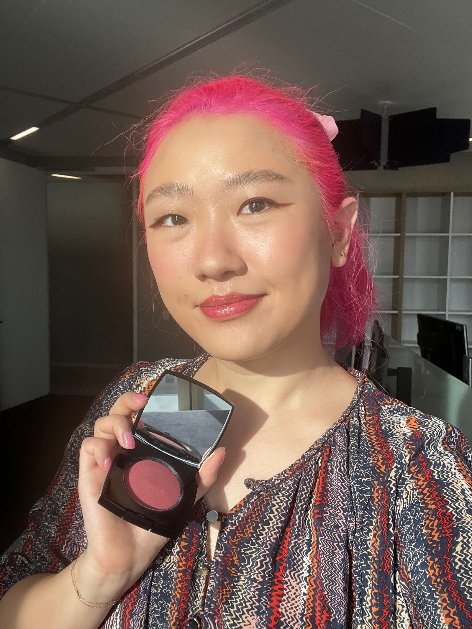 Woman smiling at the camera and holding a blush compact in her hand