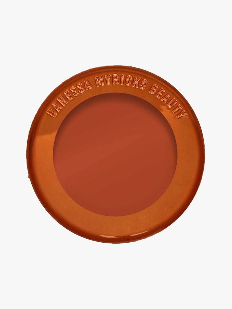 Danessa Myricks Beauty Yummy Skin Blurring Balm Powder Flushed top view of a bronze and transparent jar of terracotta blush balm on light gray background