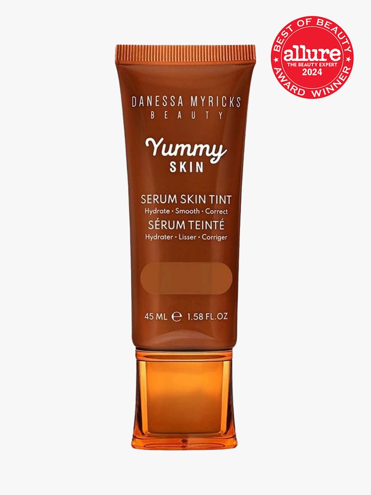 Danessa Myricks Beauty Yummy Skin Serum Skin Tint brown tube with orange cap on a light gray background with red Allure...