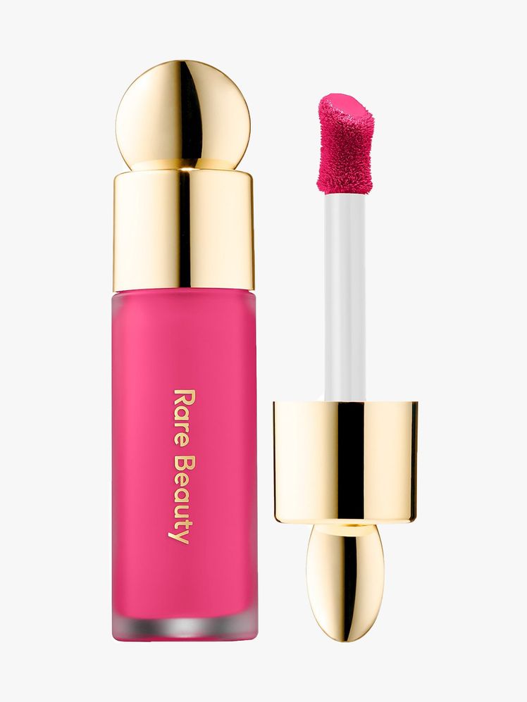 Rare Beauty Soft Pinch Liquid Blush vial of hot pink liquid blush with gold bauble cap and wand to the side on light...