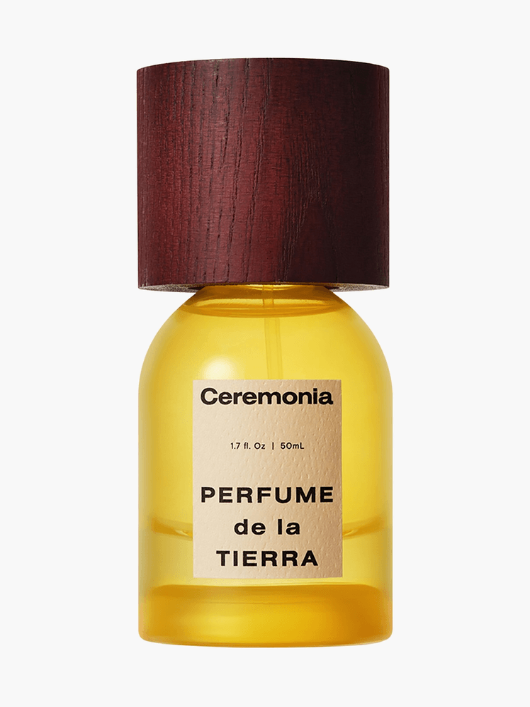 Perfume De La Tierra in branded transparent yellow bottle with wooden cap on light gray background